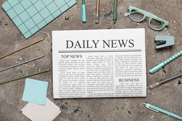 Newspaper with eyeglasses and stationery on grey grunge background