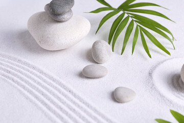 Zen garden stones and green leaves on white sand with pattern
