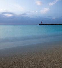 turquoise water island beach with yellow sand a lighthouse on the breakwater and silk effect water