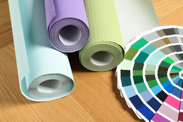 Different wallpaper rolls and color palette samples on wooden table