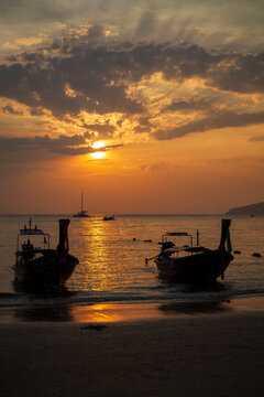 Beautiful view of silhouette of long-tail boats, sea and stunning orange sky during sunset at the Railay West Beach in Railay, Krabi, Thailand.