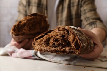 Man holding loaf of fresh broken bread on white table, closeup
