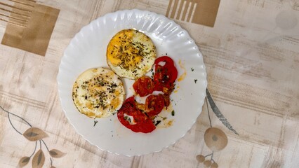Round fried eggs with tomatoes on a white plate on a tablecloth. Close-up