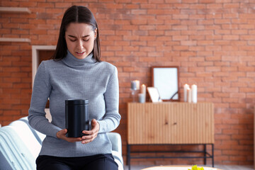 Mourning young woman with mortuary urn at funeral