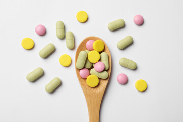Different vitamin pills in wooden spoon on white background, top view
