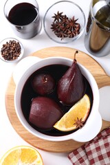 Tasty red wine poached pears in pot, orange and spices on white table, flat lay