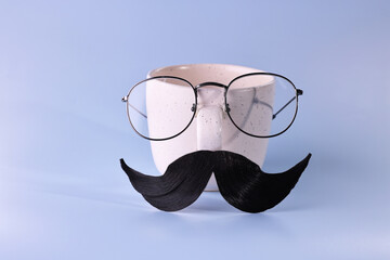 Man's face made of artificial mustache, glasses and cup on light blue background