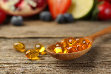 Vitamin pills in spoon on wooden table, closeup