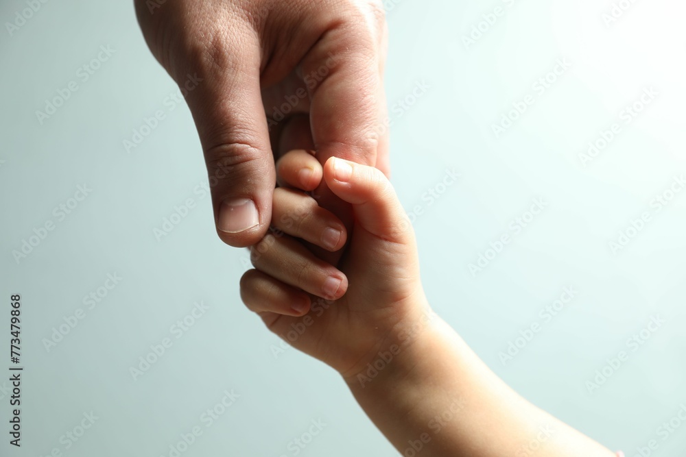 Wall mural Father and child holding hands on light blue background, closeup - Wall murals