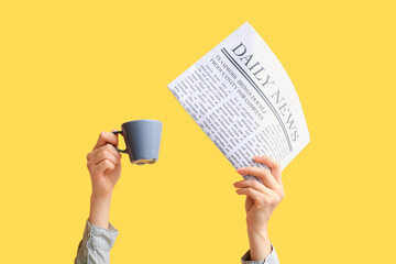 Female hands with newspaper and cup of coffee on yellow background