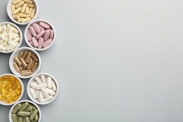 Different vitamin pills in bowls on grey background, flat lay. Space for text