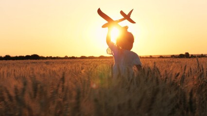 Adorable female kid silhouette running with aircraft toy at cinematic sunset sunrise wheat field back view. Happy little girl child playing pilot game with plane plaything enjoy childhood at dusk - obrazy, fototapety, plakaty