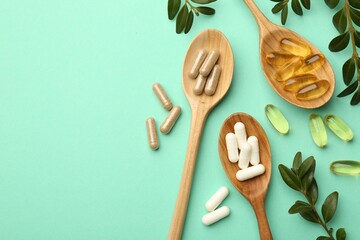 Different vitamin capsules in spoons and leaves on turquoise background, flat lay. Space for text