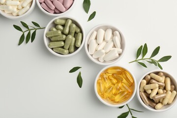 Different vitamin capsules in bowls and leaves on white background, flat lay. Space for text