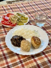 One glass of water. Tomatoes, apples, pickles, sprouted mung beans on white plate on colored background. The second plate is filled with rice, homemade cutlets and fried ordinary mushrooms. Close-up.