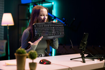 Young influencer testing mechanical keyboard while doing review in personal studio to see if price is justified. Gen Z media star showcasing computer peripheral features to audience - obrazy, fototapety, plakaty