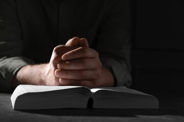 Religion. Christian man praying over Bible at table, closeup