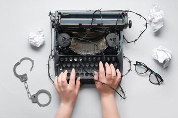 Female hands with vintage typewriter, barbed wire and handcuffs on white background. Printing ban concept