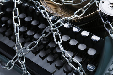 Vintage typewriter with chains, closeup. Printing ban concept