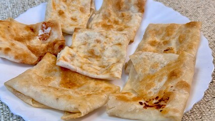 Fried pancakes-envelopes with cottage cheese, in form of envelopes in pita bread on white plate on table against background of a tablecloth