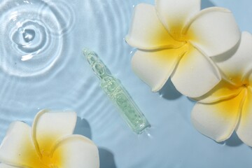 Skincare ampoule and beautiful plumeria flowers in water on light blue background, flat lay