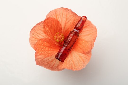 Skincare ampoules and hibiscus flower with water drops on white background, top view