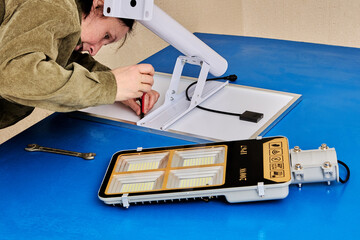 Assembling stand alone solar street light, an electrician attaches solar module and LED luminary to...