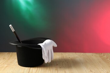 Magician's hat, wand and gloves on wooden table against color background, space for text