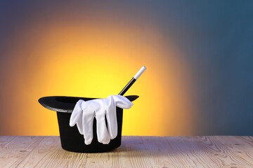 Magician's hat, wand and gloves on wooden table against color background, space for text