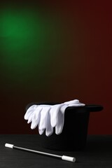 Magician's hat, wand and gloves on black wooden table against dark background, space for text