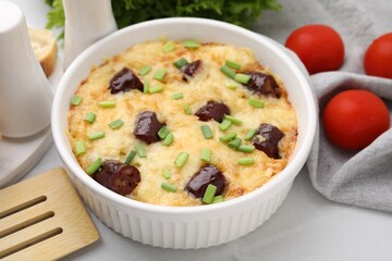 Tasty sausage casserole with green onions in baking dish served on white tiled table, closeup