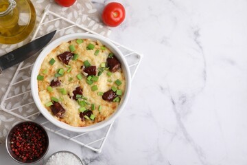 Tasty sausage casserole in baking dish, knife and ingredients on white marble table, flat lay. Space for text