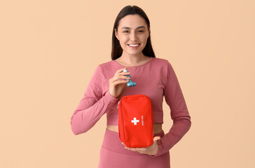 Sporty young woman with inhaler and first aid kit on beige background