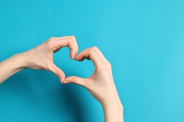 Woman showing heart gesture with hands on light blue background, closeup. Space for text