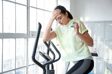 Sporty young woman with inhaler having asthma attack on treadmill in gym