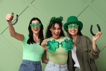 Beautiful young women with decorative glasses and horseshoes on green background. St. Patrick's Day...