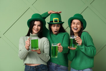 Beautiful young women in leprechaun hats with glasses of beer on green background. St. Patrick's...