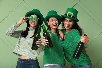 Beautiful young women in leprechaun hats with bottles of beer on green background. St. Patrick's...