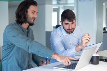 Travail en équipe. deux collègues travaillent ensemble dans un bureau sur le même projet. Ils discutent et sont assis devant un ordinateur portable. - 773484255