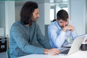 Travail en équipe. deux collègues travaillent ensemble dans un bureau sur le même projet. Ils discutent et sont assis devant un ordinateur portable. - 773484257
