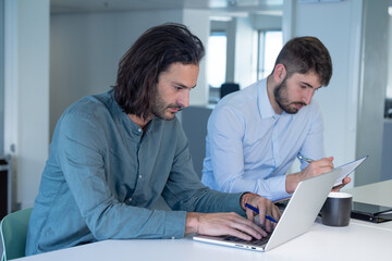 Travail en équipe. deux collègues travaillent ensemble dans un bureau sur le même projet. Ils discutent et sont assis devant un ordinateur portable. - 773484290