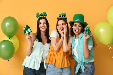 Beautiful young women with gift boxes and air balloons on yellow background. St. Patrick's Day...