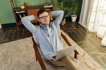 A relaxed professional reclines in a mid-century modern chair, laptop on his knees, embodying a...
