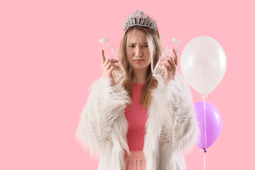 Young woman with hangover and water bottles after Birthday party on pink background