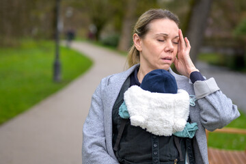 Exhausted and stressed woman holding and carrying her baby in a baby carrier