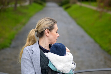 Exhausted woman holding and carrying her baby in a baby carrier and looking to side