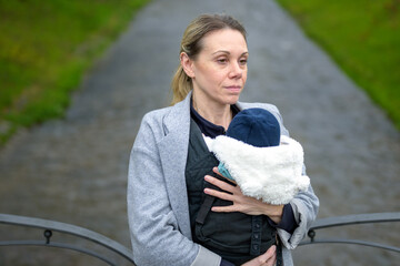 Exhausted woman holding and carrying her baby in a baby carrier