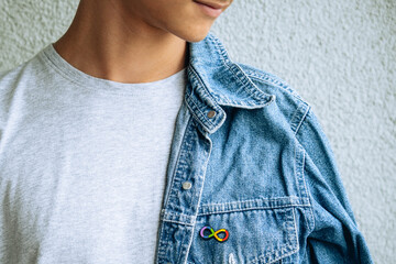 Teenage boy with autism infinity rainbow symbol sign metallic pin brooch on denim jacket. World autism awareness day, autism rights movement, neurodiversity, autistic acceptance movement - obrazy, fototapety, plakaty