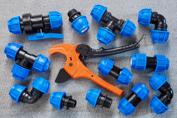 A collection of blue polyethylene pipe fittings is neatly arranged alongside an orange PVC pipe cutter, possibly during a plumbing project.