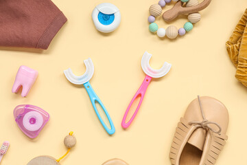 Baby clothes with toothbrushes, dental floss and toys on beige background